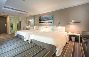 Een hotelkamer met twee bedden, een bureau met lamp, een kleine prullenbak en een schilderij aan de muur.