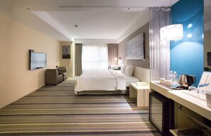 Una habitación de hotel con una cama grande, un escritorio con lámpara, televisión y un minibar.