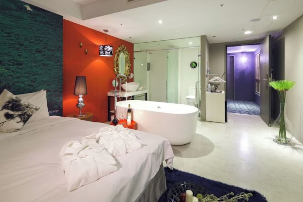 A modern hotel room with a large bed, a round bathtub, and a separate bathroom.