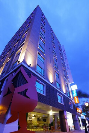 Un hotel moderno de gran altura con múltiples pisos, amplias ventanas y una entrada destacada con un elemento arquitectónico único que recuerda a una flor o una estrella.