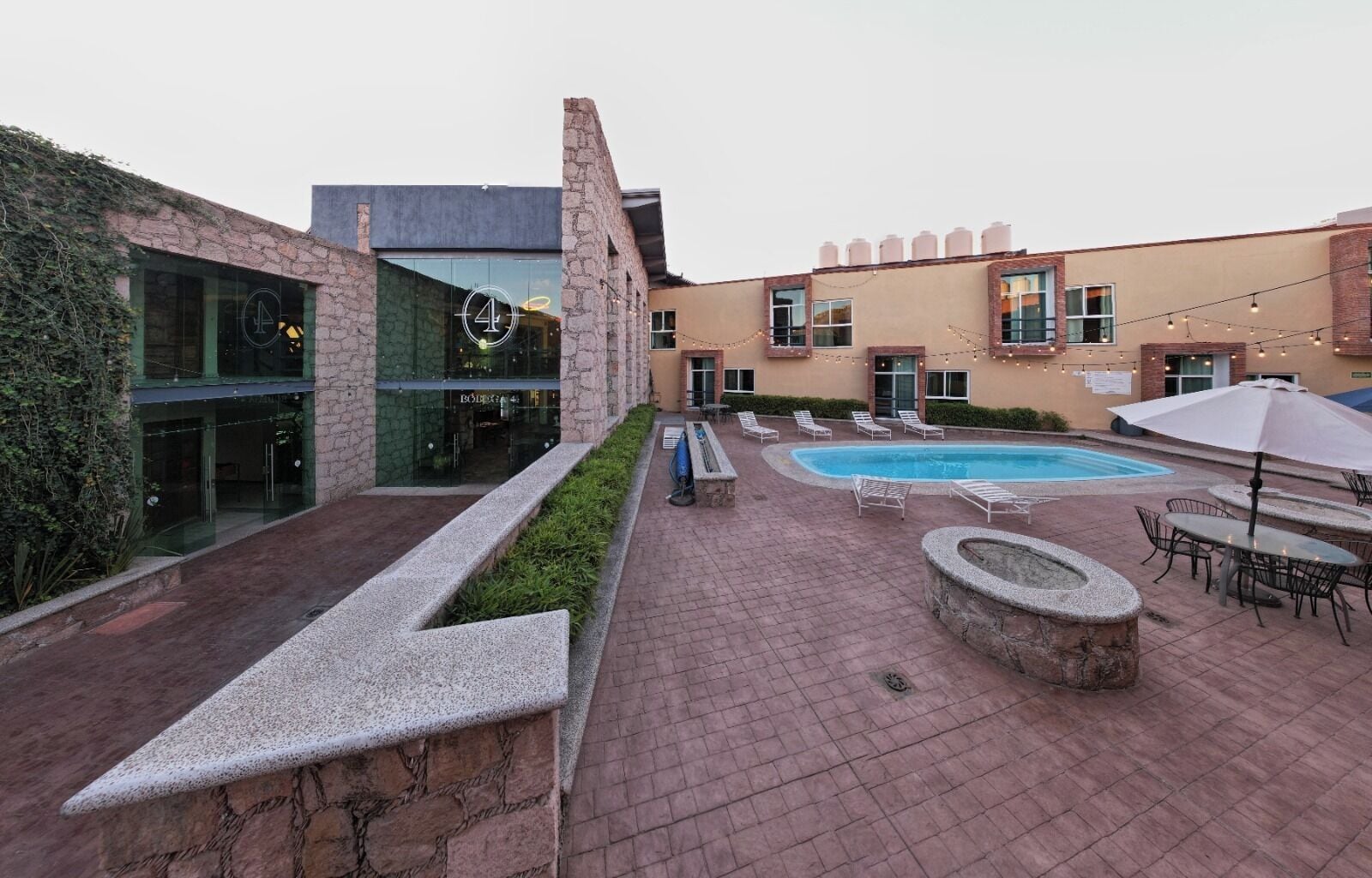 A courtyard with a swimming pool, outdoor seating, and a building with a stone facade.