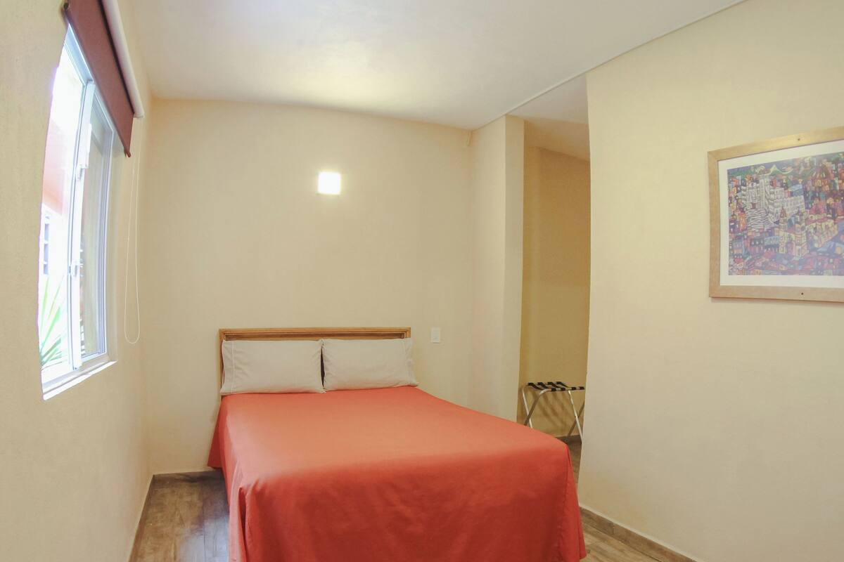 Un dormitorio pequeño y ordenado con una cama individual, un ventanal y un cuadro en la pared.