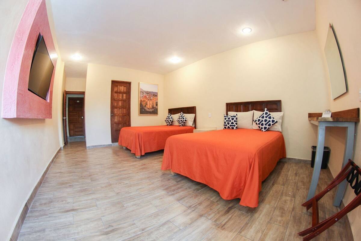 Habitación de hotel con dos camas, suelo de madera, una puerta, un cuadro y una mesita.