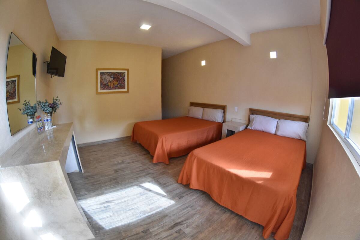 Habitación de hotel con dos camas, un espejo grande, un cuadro en la pared y una ventana con cortinas.