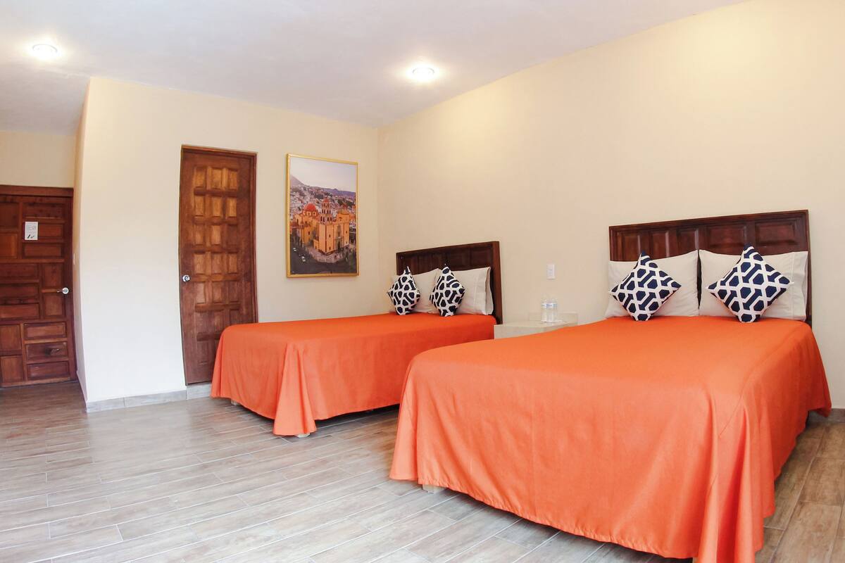 Habitación de hotel con dos camas, suelo de madera, un cuadro en la pared y una puerta.