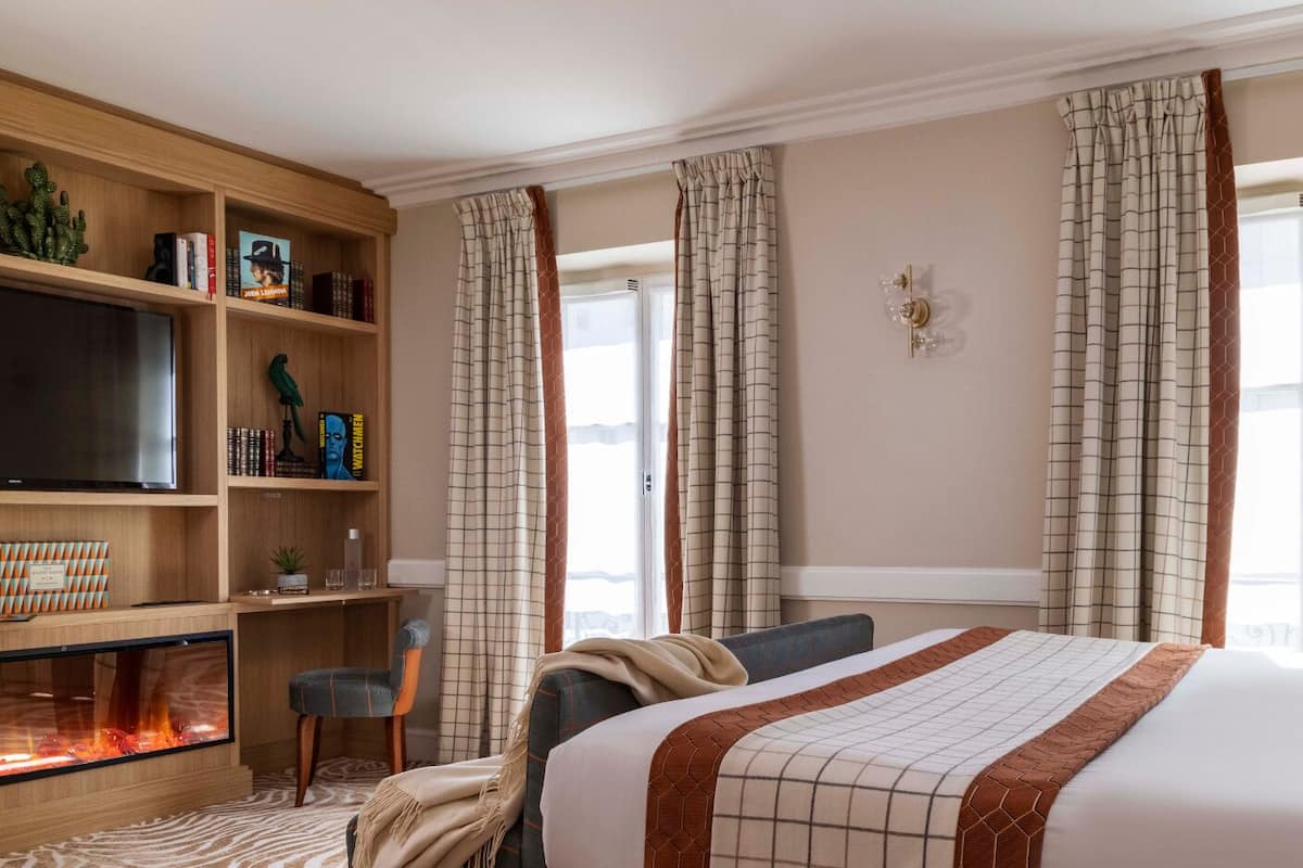 Een hotelkamer met een bed, een televisie, een boekenplank en een open haard.