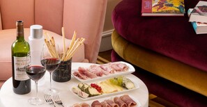 A table with a bottle of wine, glasses, a plate of meats, cheese, and a book on a plush sofa. - Hôtel Sleeping Belle - Gare de Lyon Bastille (Paris)