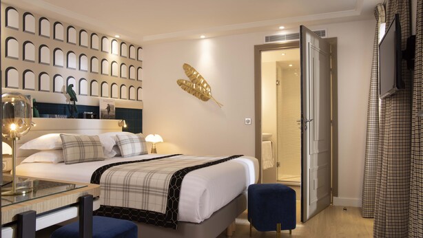 A modern hotel room with a neatly made bed, a glass table, and a blue chair. - Hôtel Sleeping Belle - Gare de Lyon Bastille (Paris)