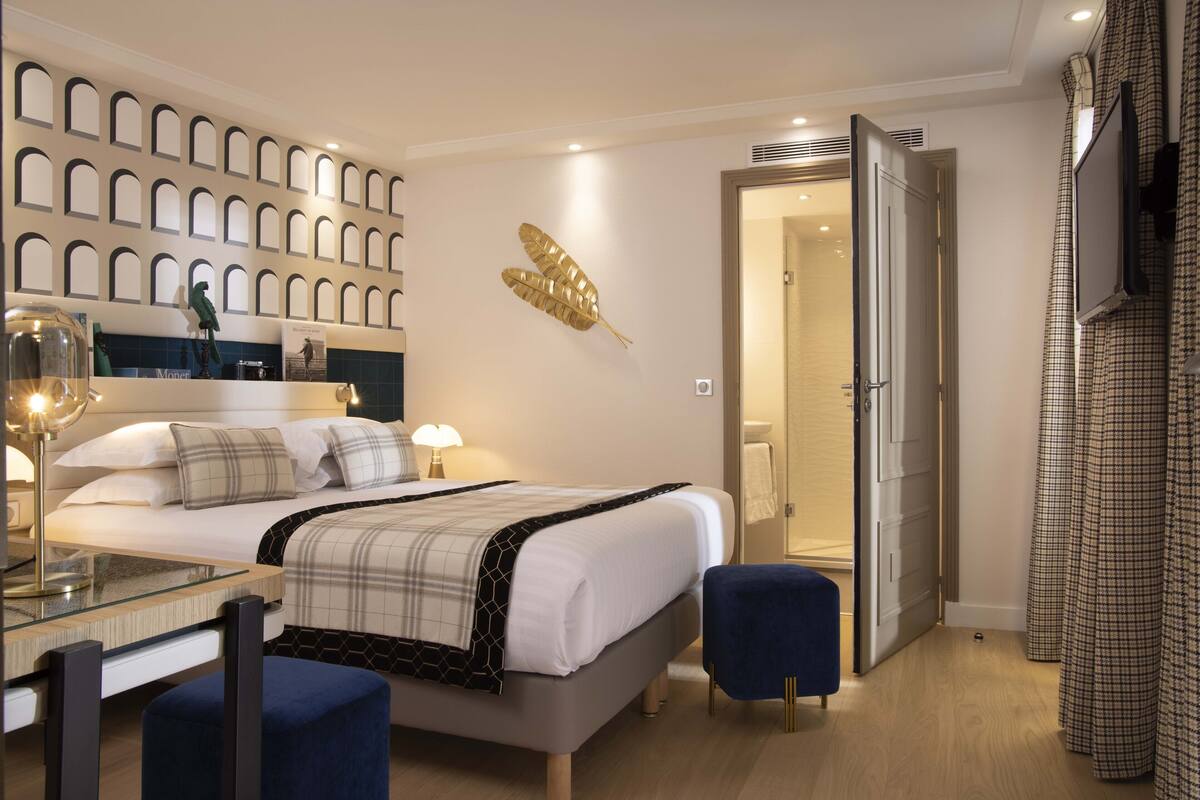 Een moderne hotelkamer met een net opgemaakt bed, een glazen tafel en een blauwe stoel.