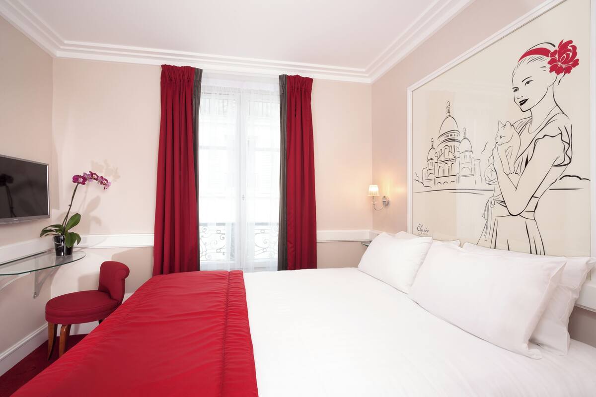 Een hotelkamer met een bed, een bureau met stoel, een televisie, een raam met gordijnen en een muur met een tekening.