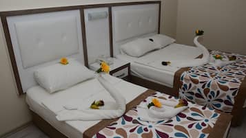 A hotel room with two beds, each with a white headboard, a bedside table, and a decorative towel with flowers.