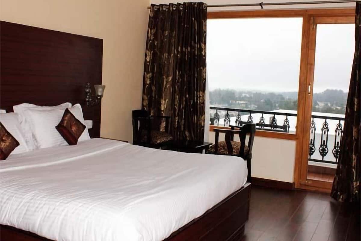 A bedroom with a large bed, a nightstand, a chair, and a view of a balcony with a railing.