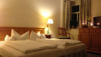 A hotel room with a large bed, a nightstand with a lamp, a wooden chair, a television, and a window with curtains.