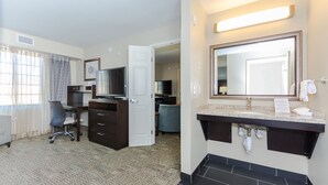 A hotel room with a desk, chair, TV, and a large mirror above the sink. - Staybridge Suites Grand Forks by IHG (Grand Forks)