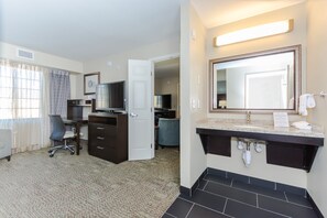 A hotel room with a desk, chair, TV, and a large mirror above the sink. - Staybridge Suites Grand Forks by IHG (Grand Forks)