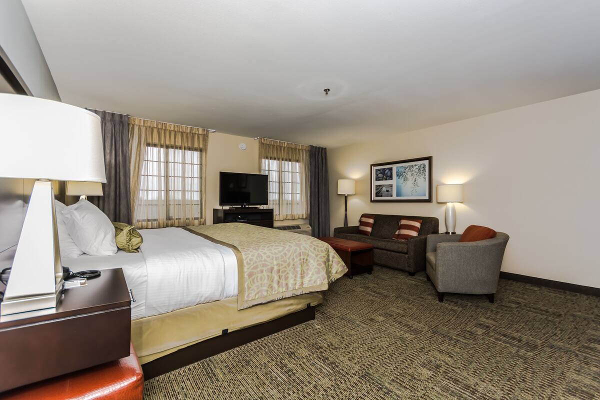 A hotel room with a bed, a desk with a lamp, a television, a sofa, and a chair.