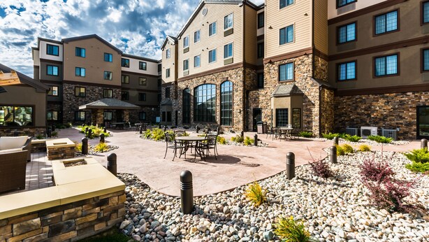 A courtyard with outdoor seating, stone walls, and a multi-story building with large windows and stone accents. - Staybridge Suites Grand Forks by IHG (Grand Forks)