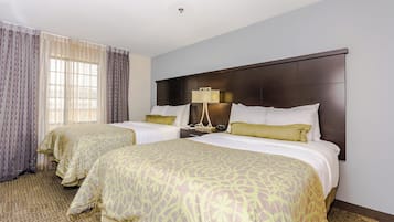 A hotel room with two beds, a nightstand with a lamp, and a window with curtains.