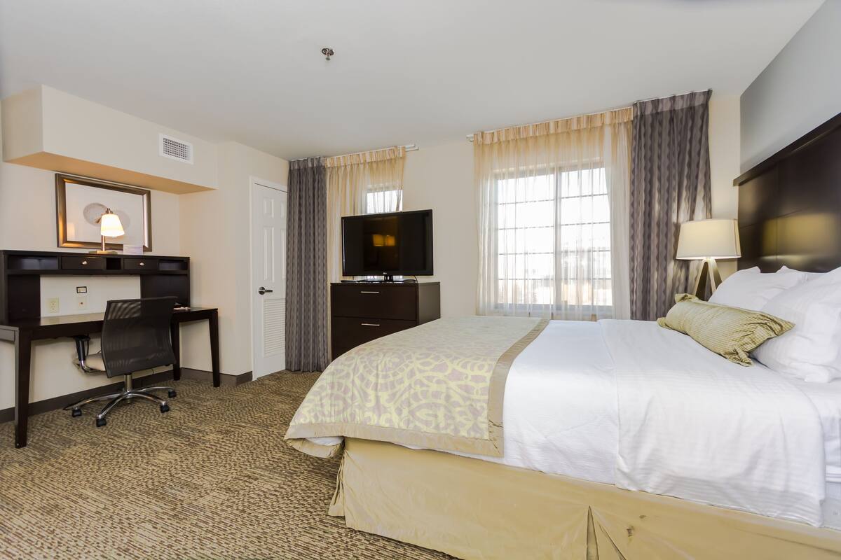 A hotel room with a bed, a desk, a television, and a window with curtains.