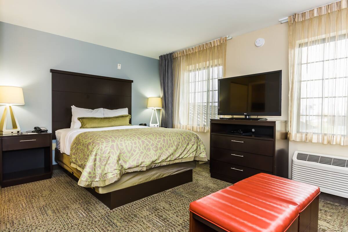 A hotel room with a bed, bedside tables, a TV, a heater, and a window with curtains.