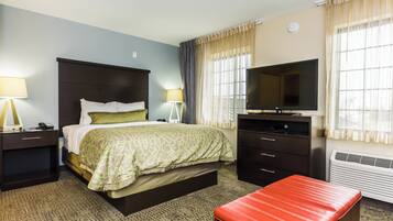 A hotel room with a bed, bedside tables, a TV, a desk, and a red bench.