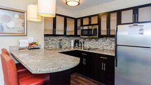 A modern kitchen with granite countertops, stainless steel appliances, and dark cabinetry. - Staybridge Suites Grand Forks by IHG (Grand Forks)
