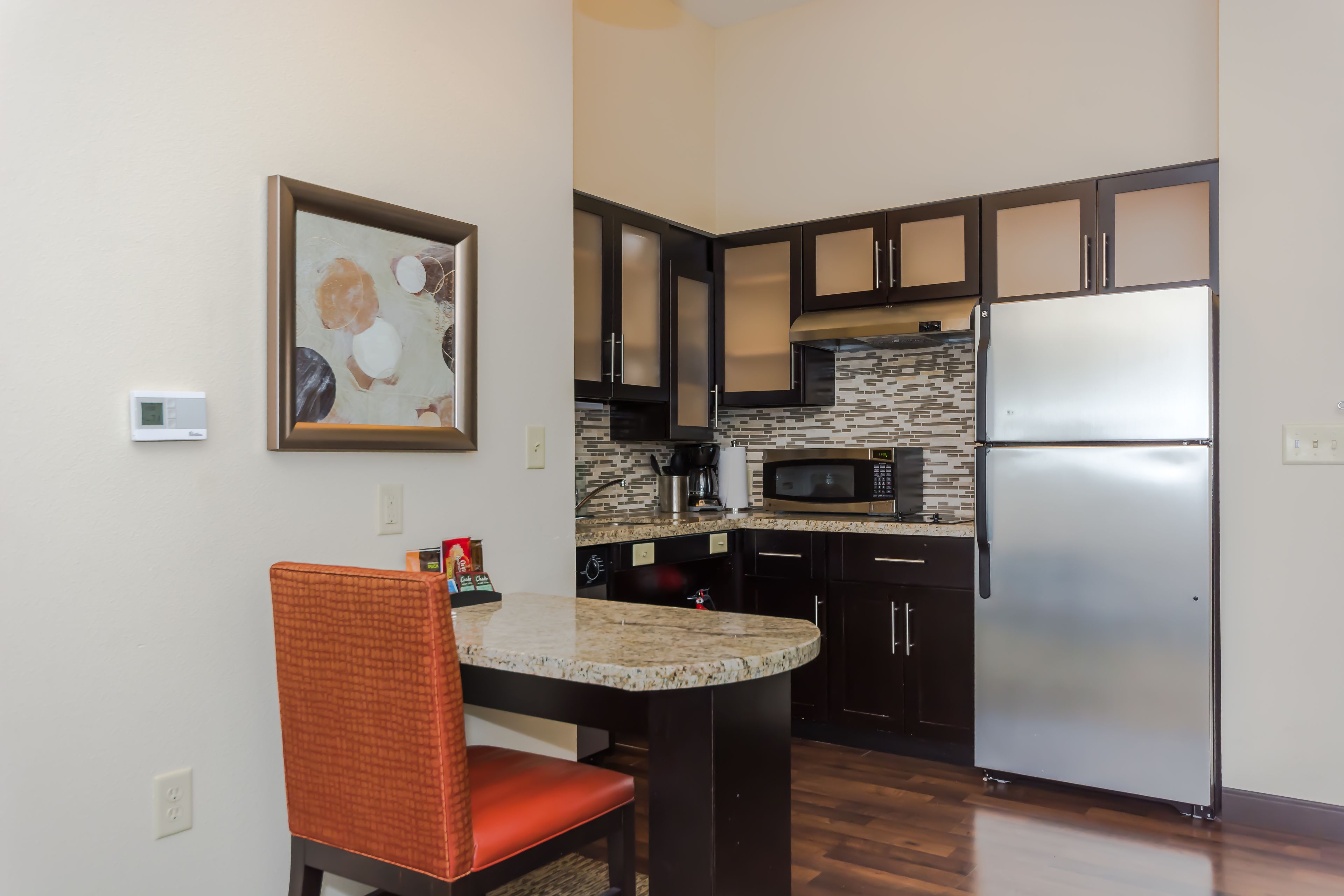 A modern kitchen with dark cabinets, a stainless steel refrigerator, a microwave, and a granite countertop.