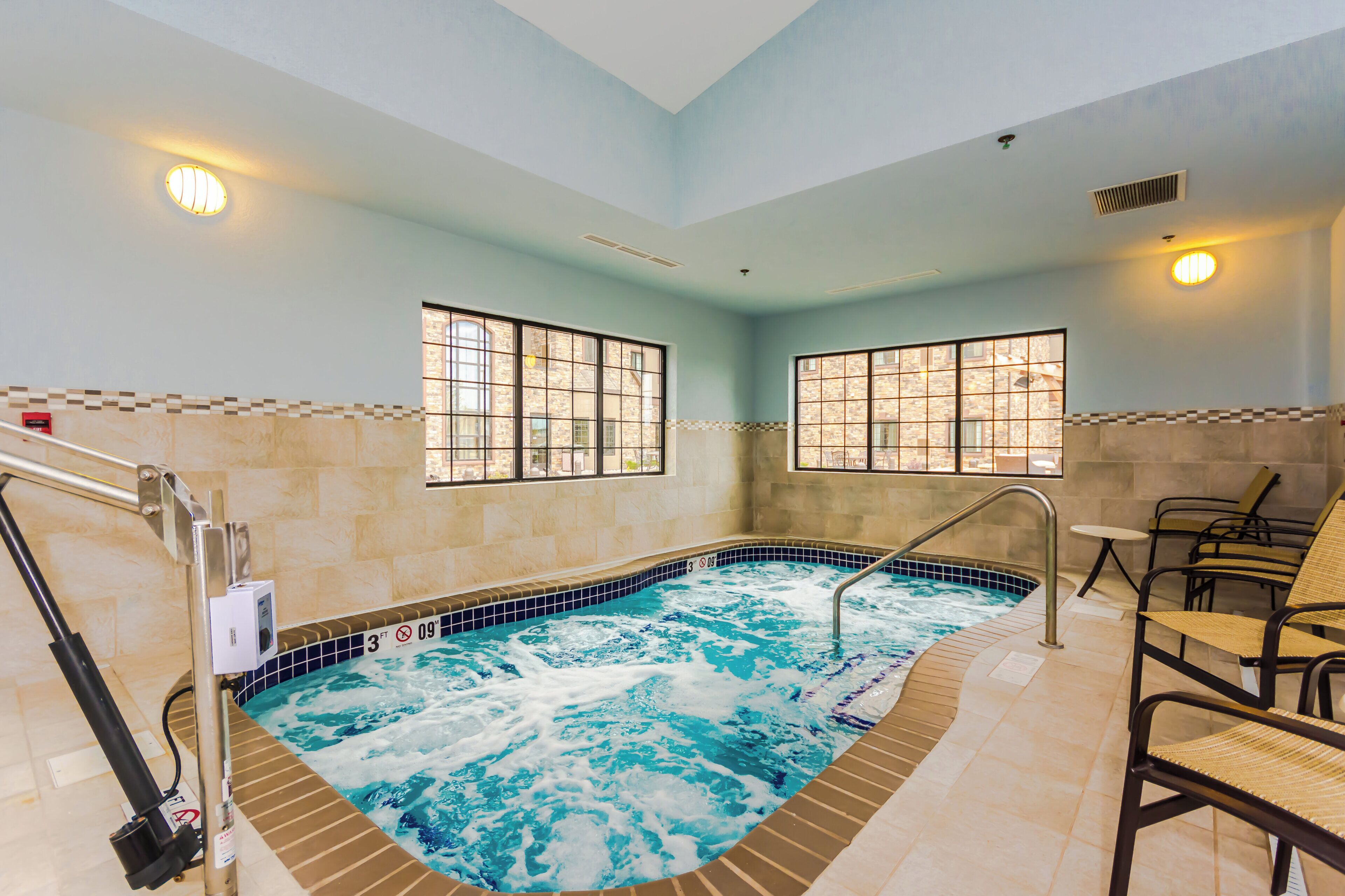 A hot tub with a tiled surround, a window with a view, and a chair.
