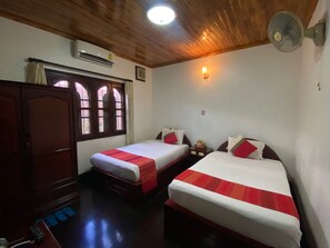 A room with two beds, a wardrobe, an air conditioning unit, a window with curtains, and a wall-mounted fan. - Vangsavath Hotel (Luang Prabang)