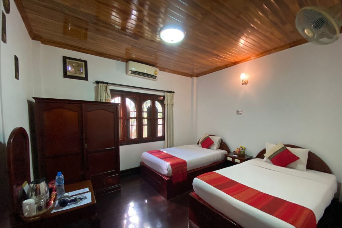 A hotel room with two beds, wooden furniture, a desk with toiletries, and a ceiling fan.
