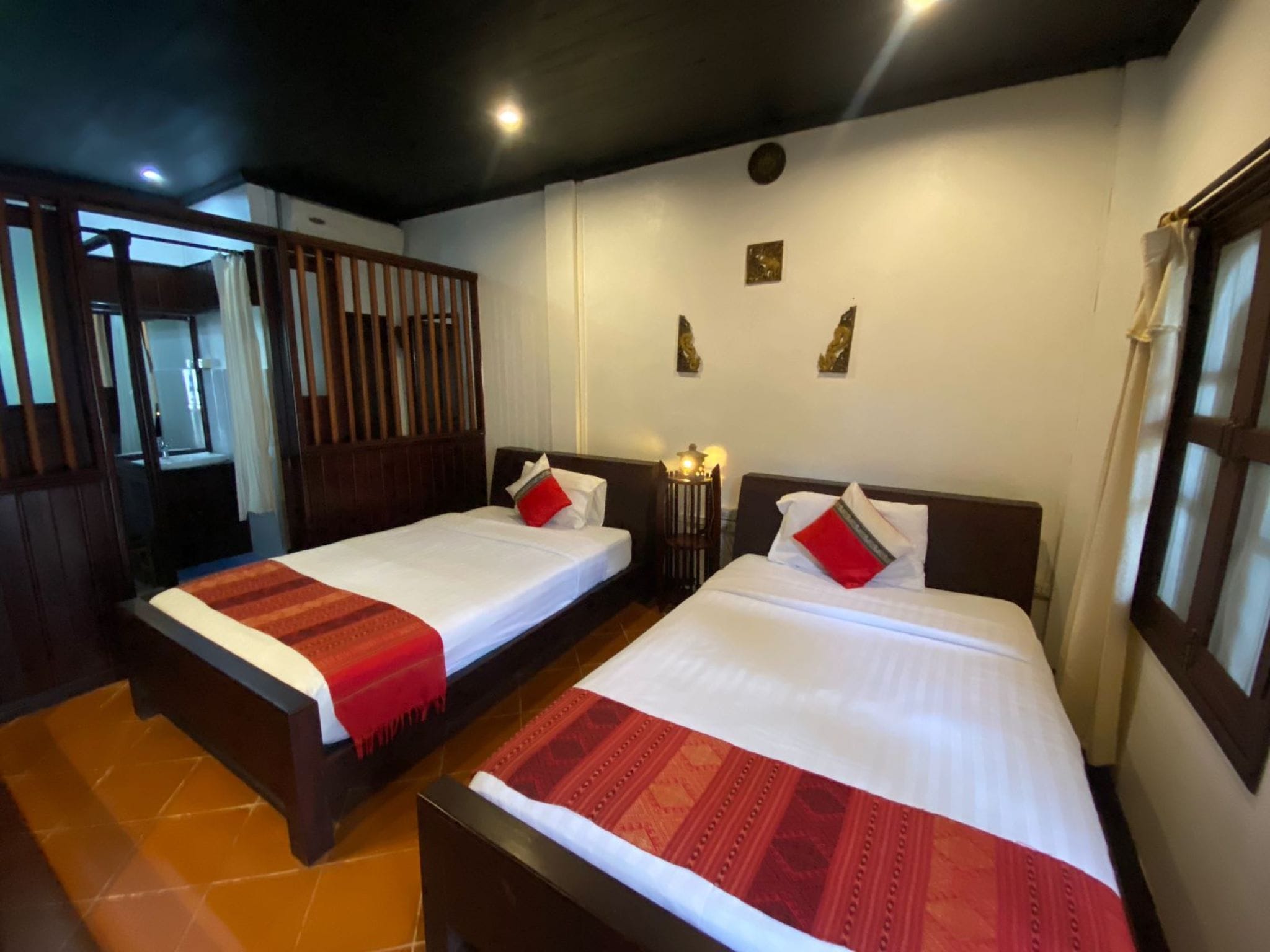 Habitación de hotel con dos camas, cada una con cubrecama rojo y blanco, cabeceros de madera y una mesita de noche con lámpara entre ellas.