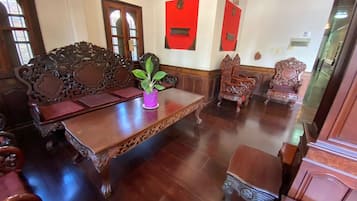 Una habitación tradicional con muebles de madera ornamentados, incluyendo un sofá y sillas, una mesa de centro de madera y un mueble bajo.