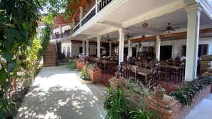 A covered outdoor dining area with brick planters and tables, a staircase leading to an upper level, and a view of the interior through the open space. - Vangsavath Hotel (Luang Prabang)