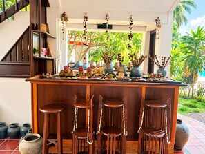 A bar area with wooden stools and a counter adorned with decorative items and plants. - Vangsavath Hotel (Luang Prabang)