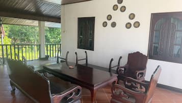 Un área de comedor al aire libre techada, con una mesa y sillas de madera, un muro decorativo con platos y vistas a la vegetación.