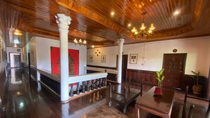 A spacious room with wooden flooring, a staircase with a balustrade, a dining area with a table and chairs, and a chandelier. - Vangsavath Hotel (Luang Prabang)