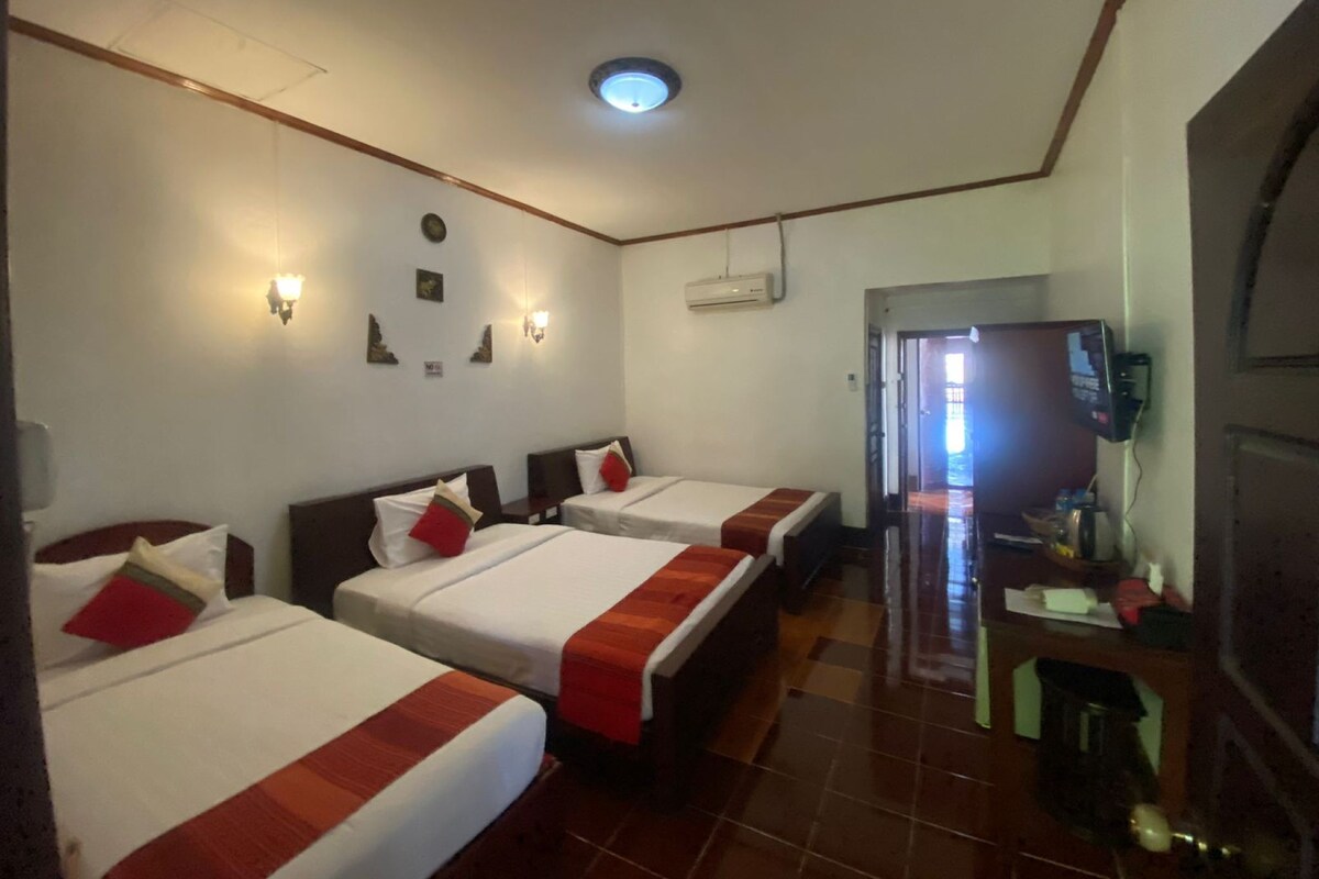 A hotel room with three beds, a TV, and a desk with a computer.