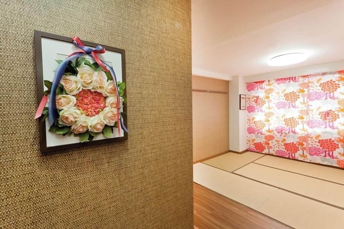 A framed floral arrangement on a textured wall, a patterned wall with a door, and a wooden floor.