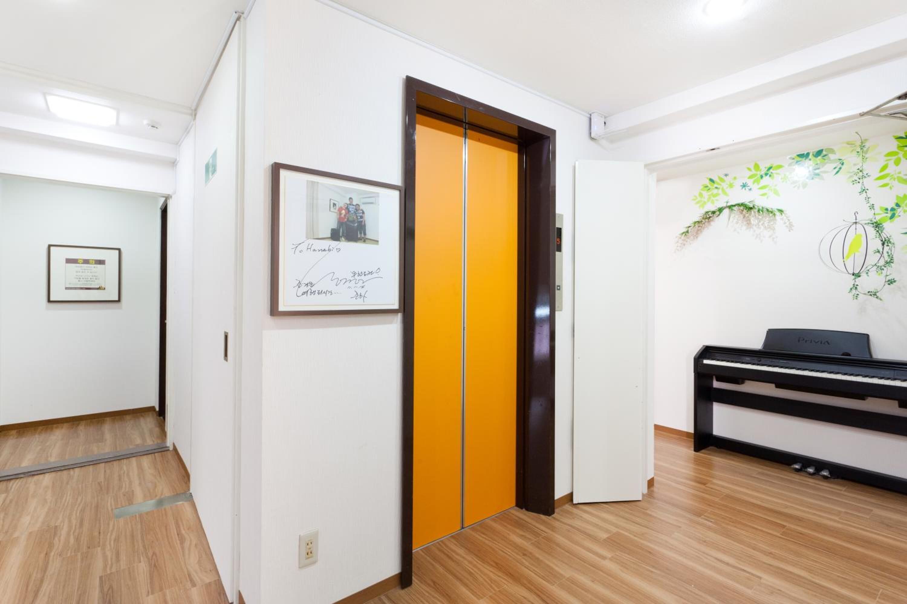 Un pasillo con piso de madera, un piano y una puerta con panel amarillo.