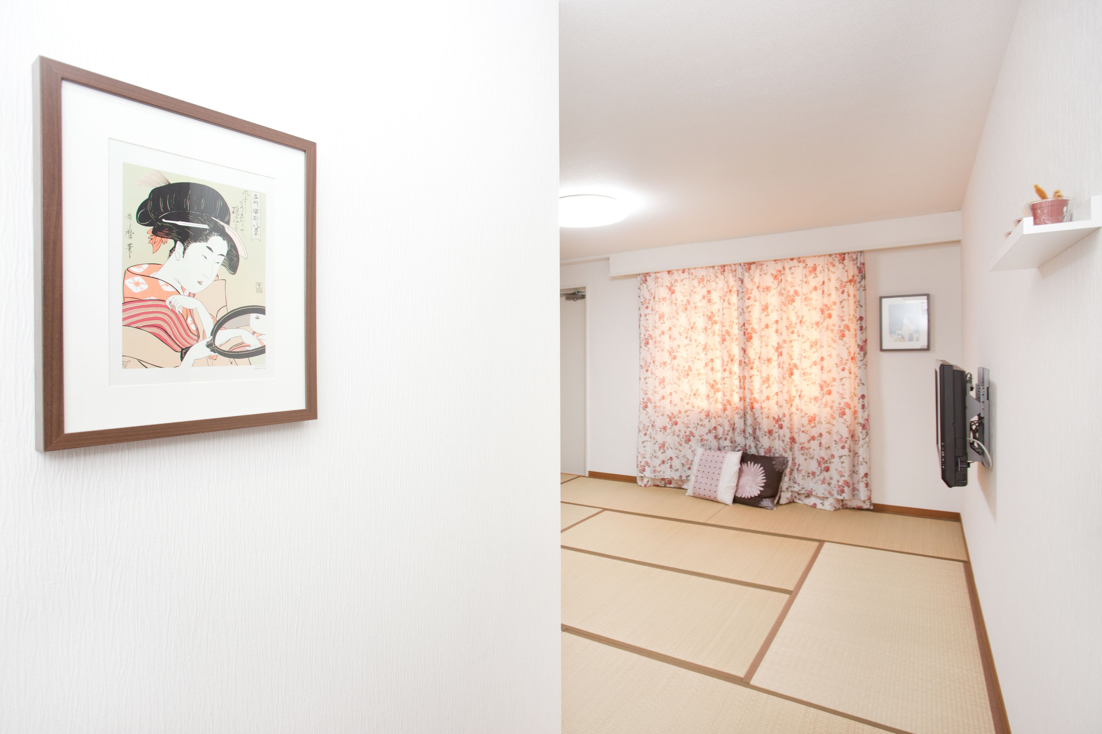 Una habitación japonesa tradicional con suelo de tatami, un biombó shoji y una obra enmarcada en la pared.