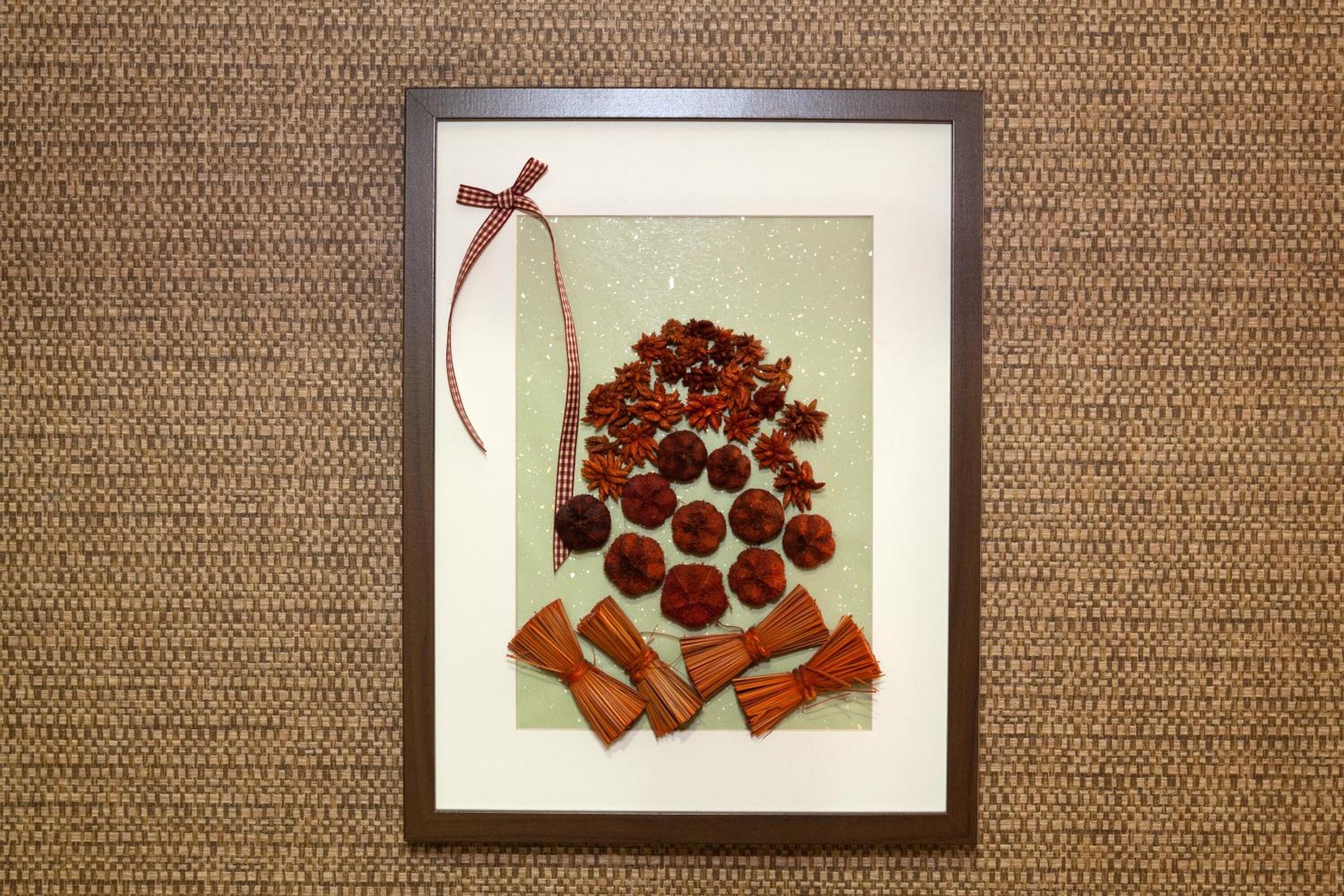 Una obra de arte enmarco con un lazo en el lado izquierdo, que muestra una colección de flores y hojas secas dispuestas en un patrón circular.