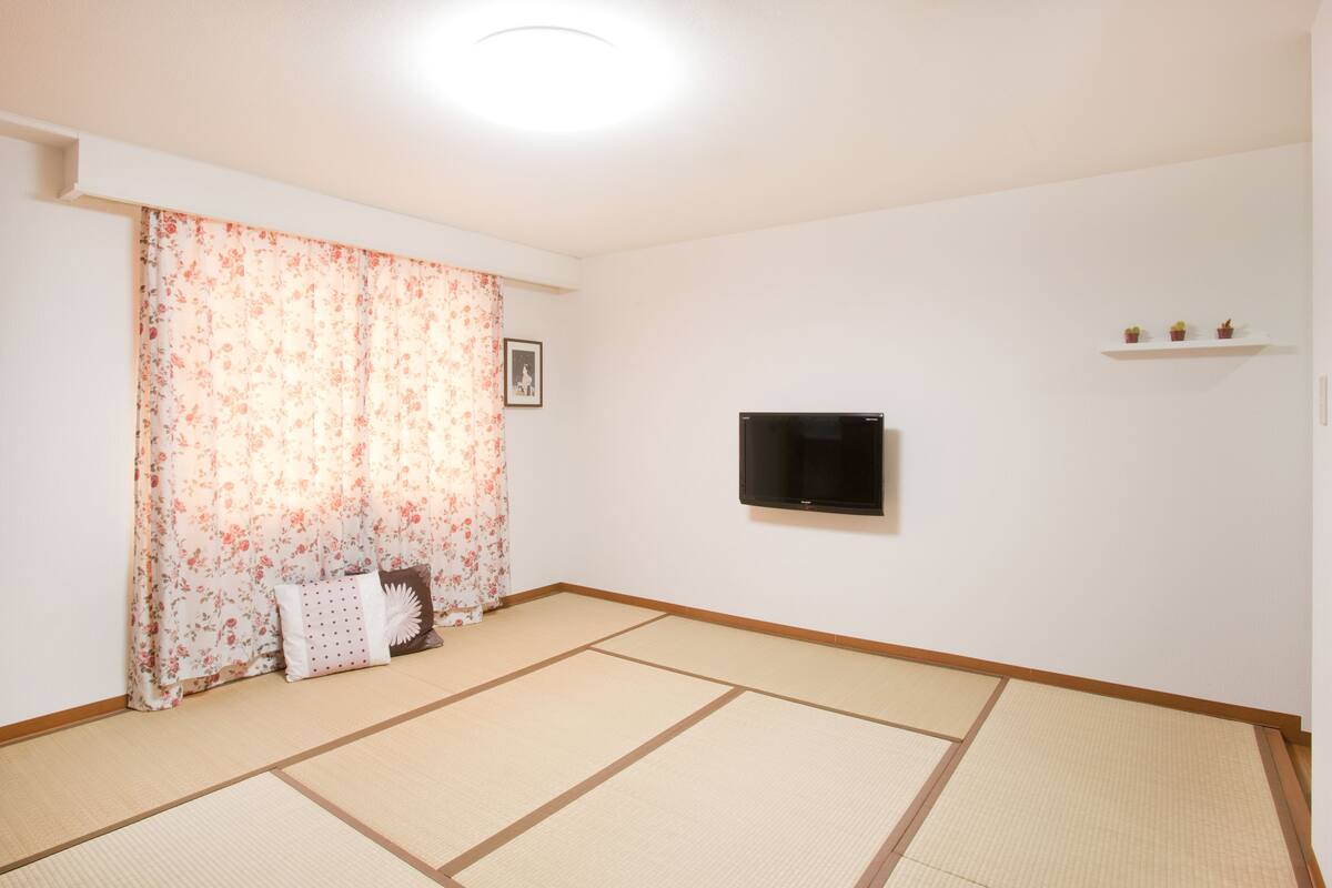 A room with tatami flooring, a television mounted on the wall, and a small shelf with decorative items.