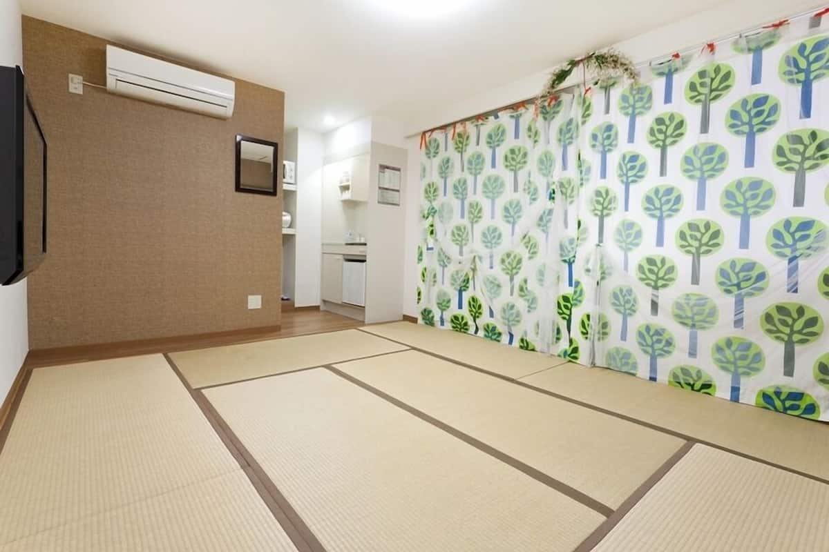 A room with tatami flooring, a sliding door with a tree pattern, and a kitchen in the background.