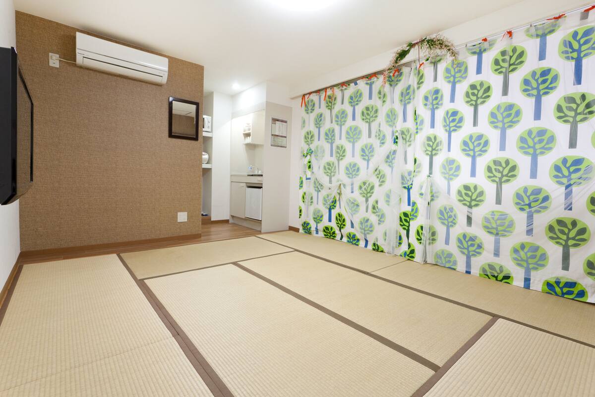 A room with tatami mats, a sliding door with a tree pattern, and a kitchen area visible through an open door.