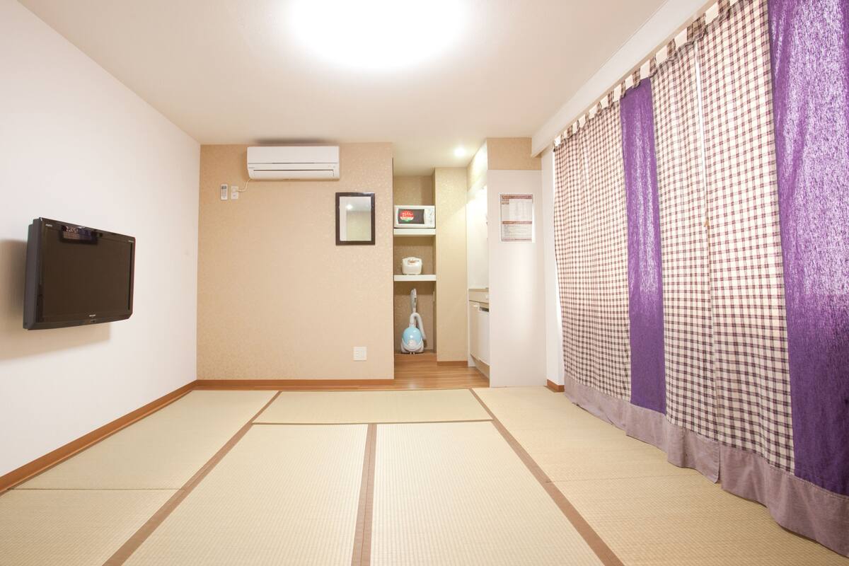 A room with tatami mats, a mounted TV, an air conditioner, and a checkered curtain.