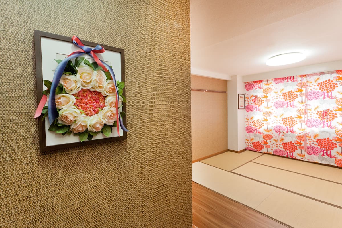 A framed floral arrangement on a textured wall, a tatami mat floor, and a colorful wall with a tree pattern.