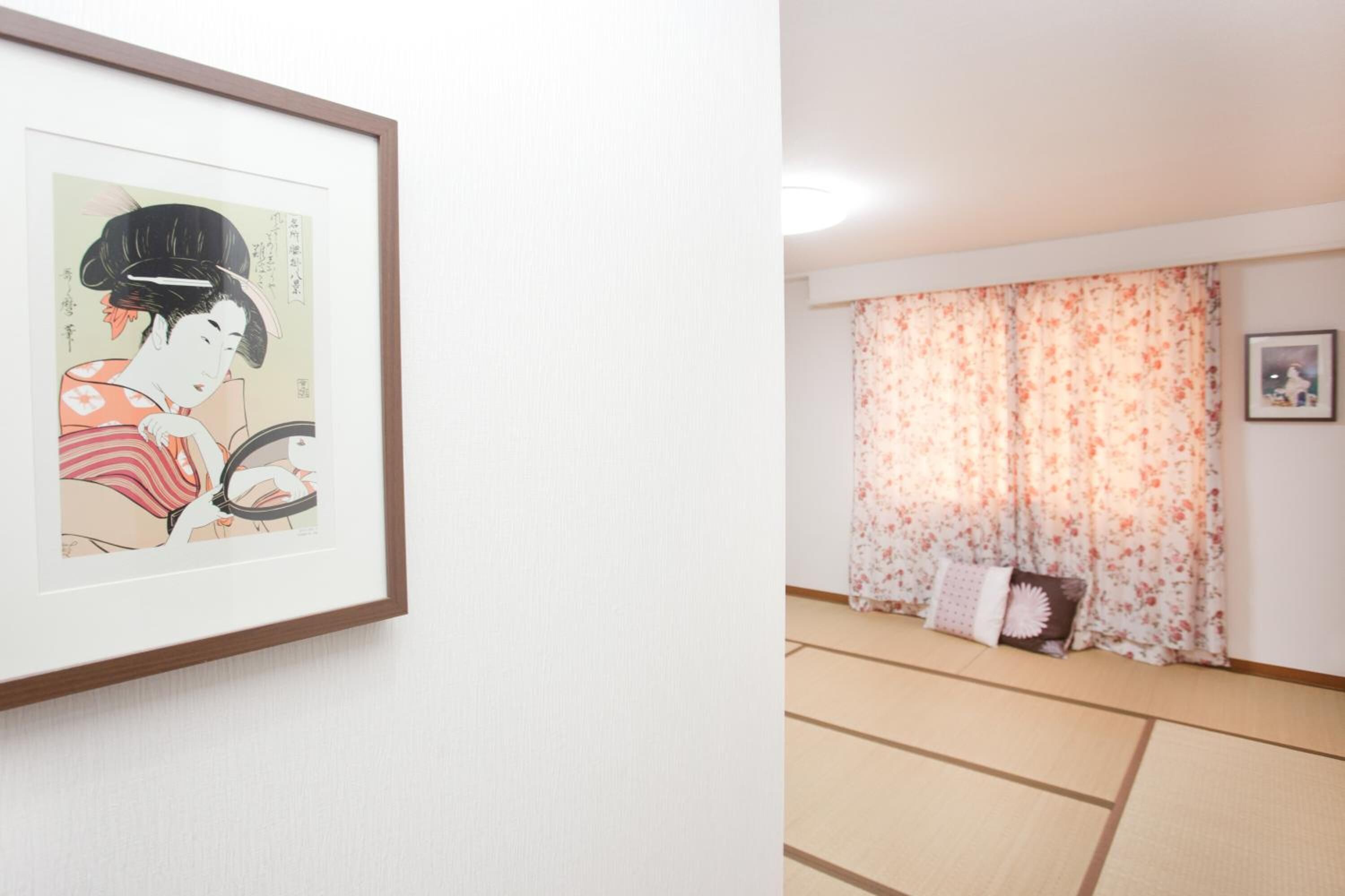 A room with tatami flooring, a framed artwork on the wall, and a floral curtain.