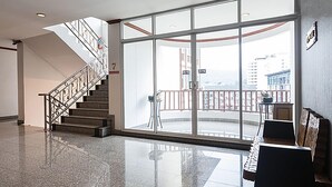 A spacious lobby with a polished floor, a staircase, and a large glass door leading to an outdoor balcony with a view of the city. - V Residence Chiangmai Hotel (Chiang Mai)
