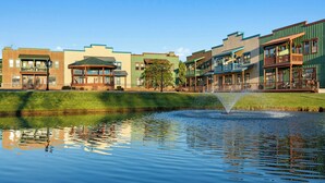 A tranquil water feature with a fountain, surrounded by multi-story buildings with varied architectural styles and a clear blue sky. - WorldMark Bison Ranch (Overgaard)