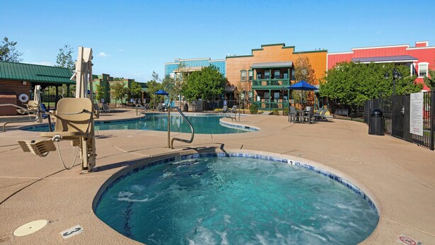 A swimming pool area with multiple pools, lounge chairs, and a building with a green roof in the background. - WorldMark Bison Ranch (Overgaard)